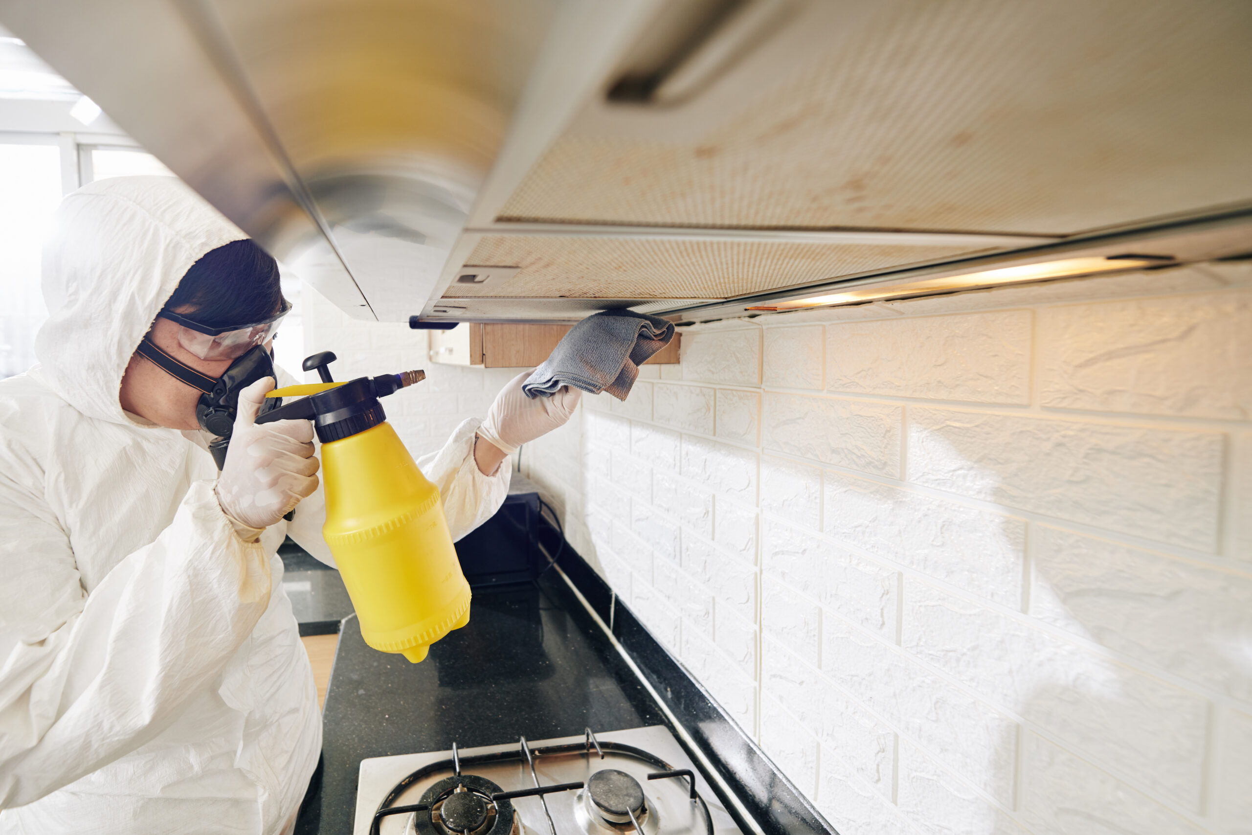 Cleaning service worker spraying detergent on greasy range hood filter in kitchen of client