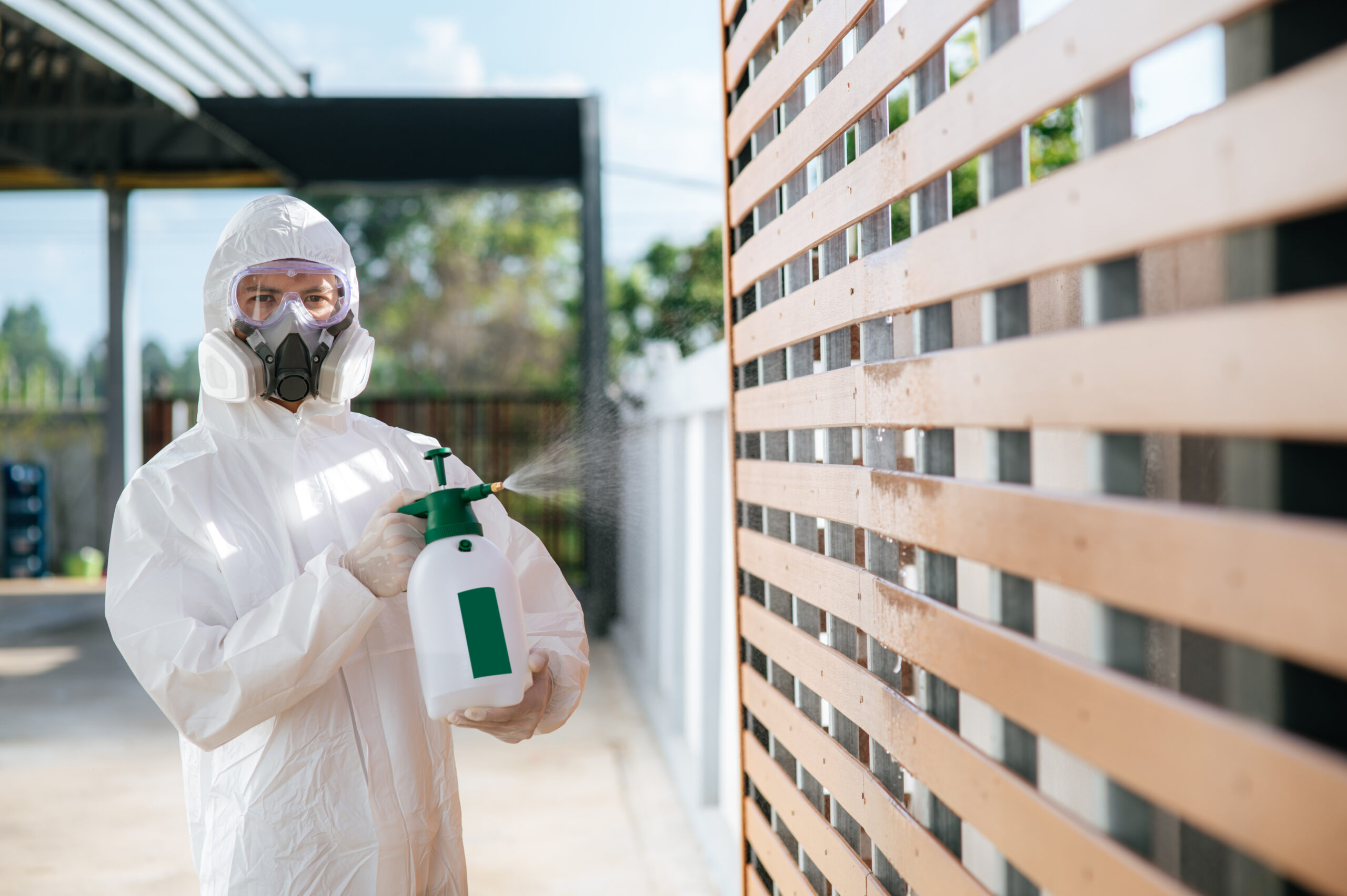Disinfection specialist staff in personal protective equipment (ppe) suit, gloves, mask and face shield, cleaning Quarantine area with a bottle of pressurized spray disinfectant to remove covid-19.