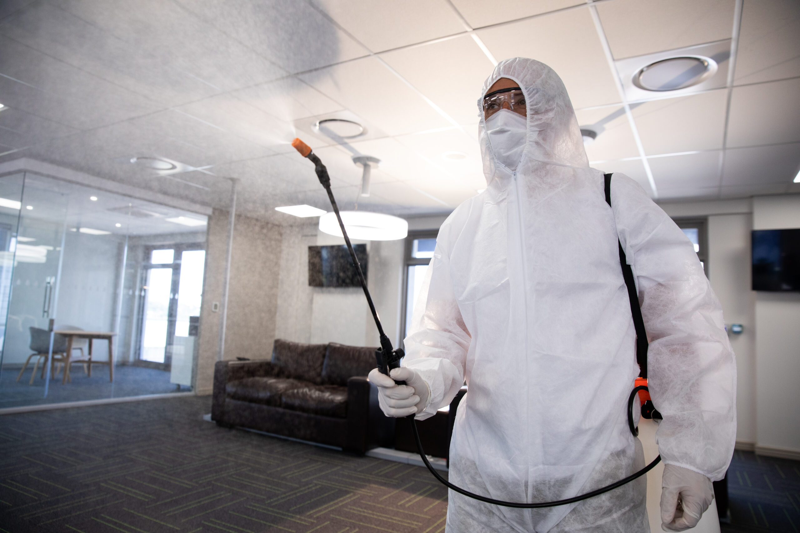 Worker wearing protective suit, face mask and gloves sanitizing office using an anti bacterial disinfectant spray. Hygiene in workplace during Coronavirus Covid 19 pandemic.