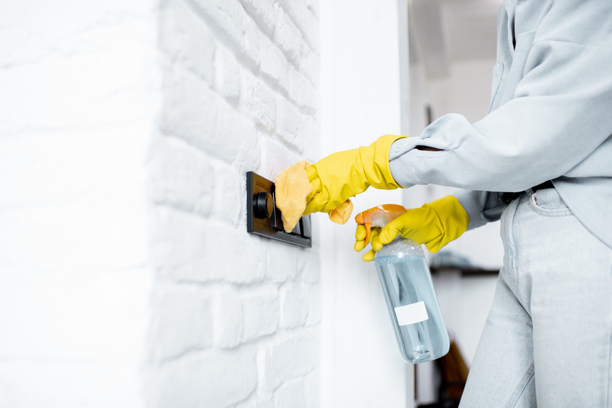 Woman in protective gloves disinfecting wall switches while cleaning at home, close-up view on hands